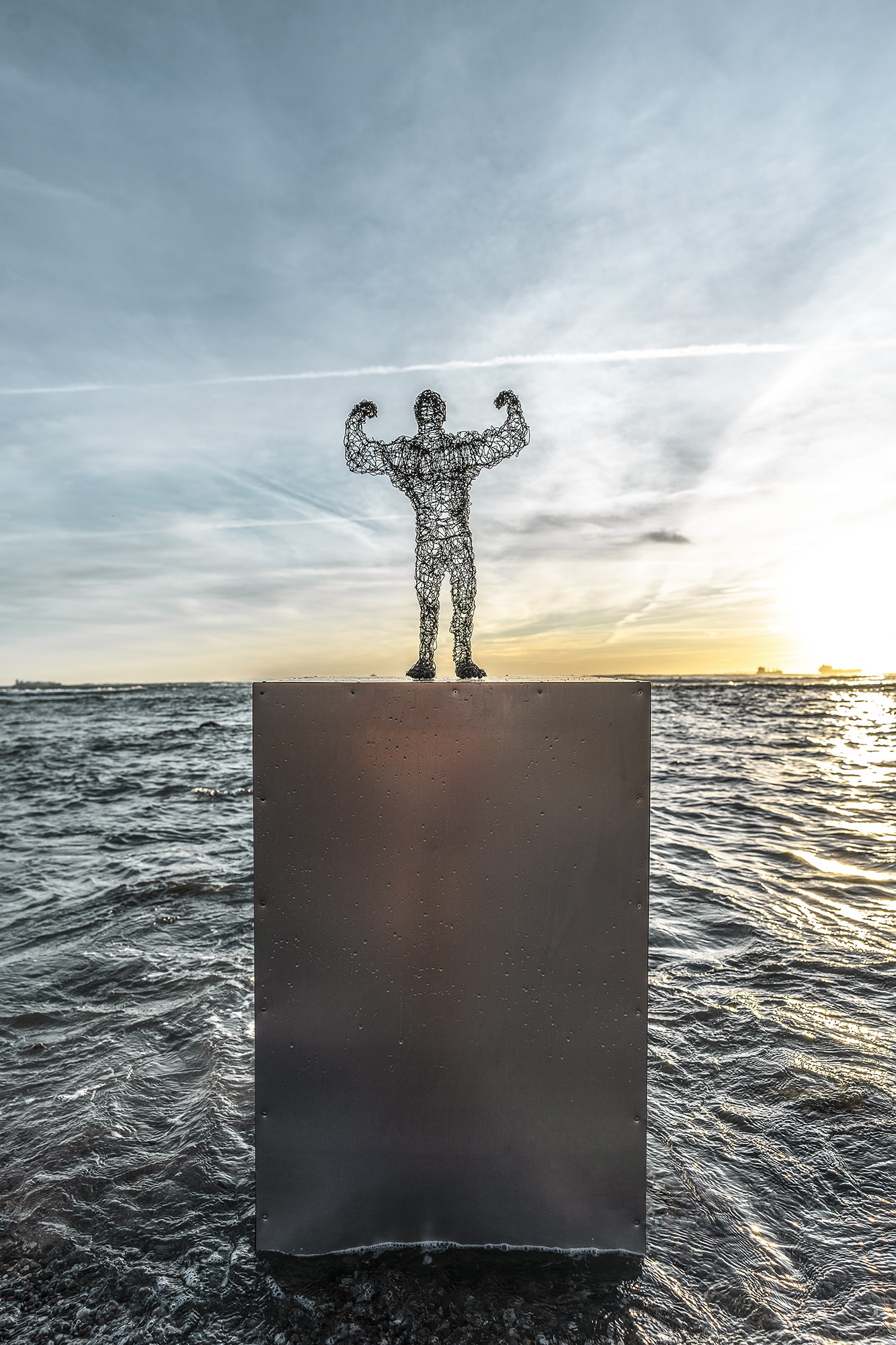 wire sculpure on a metal cube, standing from the sea in front of an orange sunset