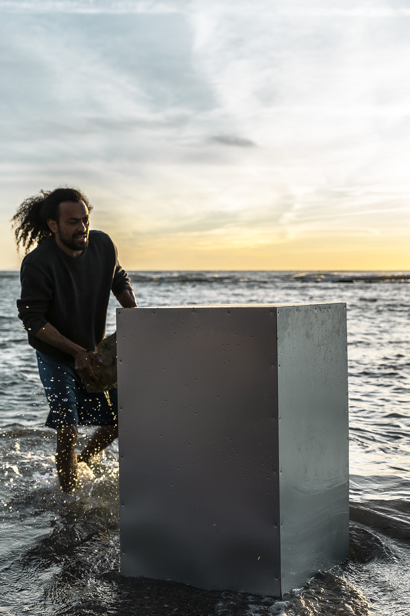 wire sculpure on a metal cube, standing from the sea in front of an orange sunset