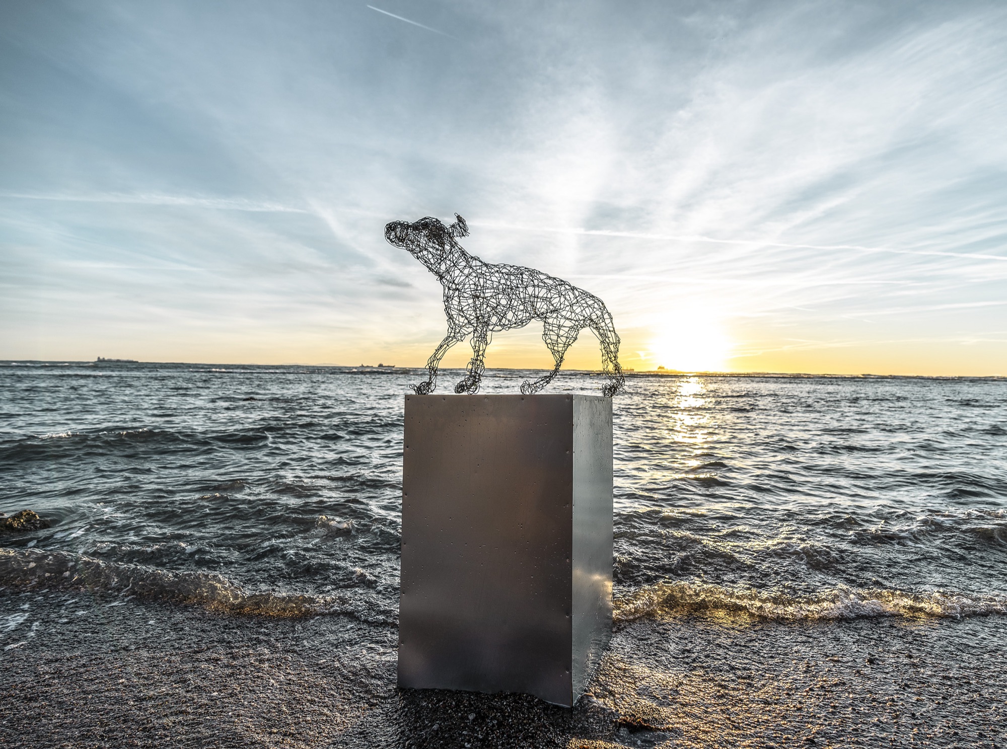 wire sculpure on a metal cube, standing from the sea in front of an orange sunset
