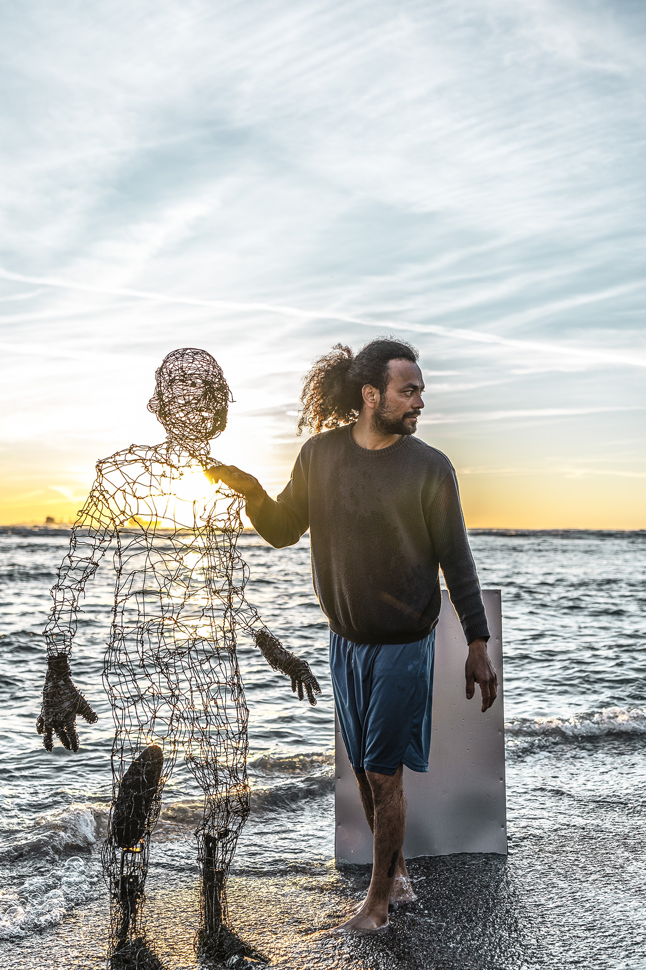wire sculpure on a metal cube, standing from the sea in front of an orange sunset