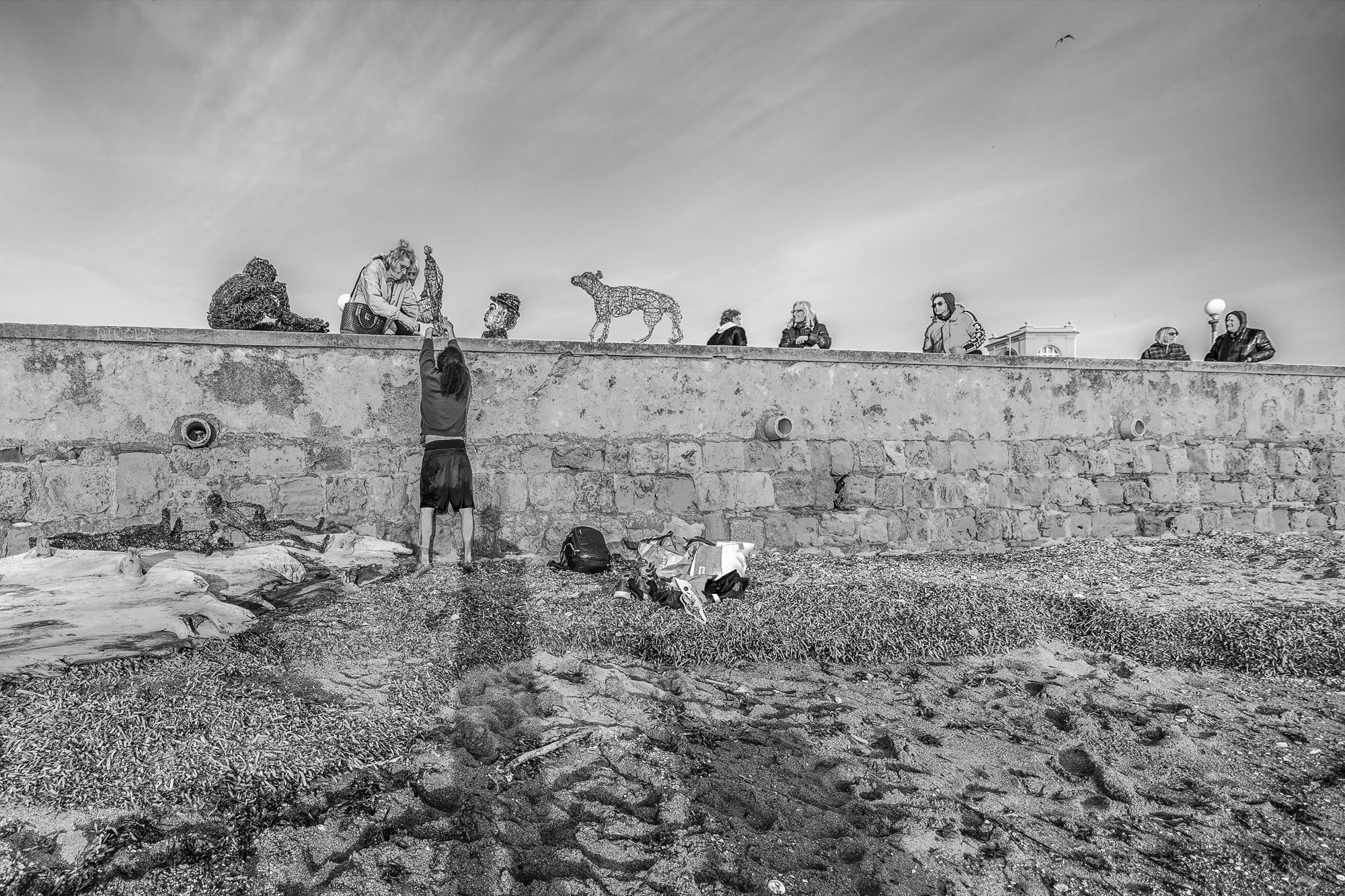 Rildson climbing a wall with sculpures on it. Passers by watching. Black and white image.