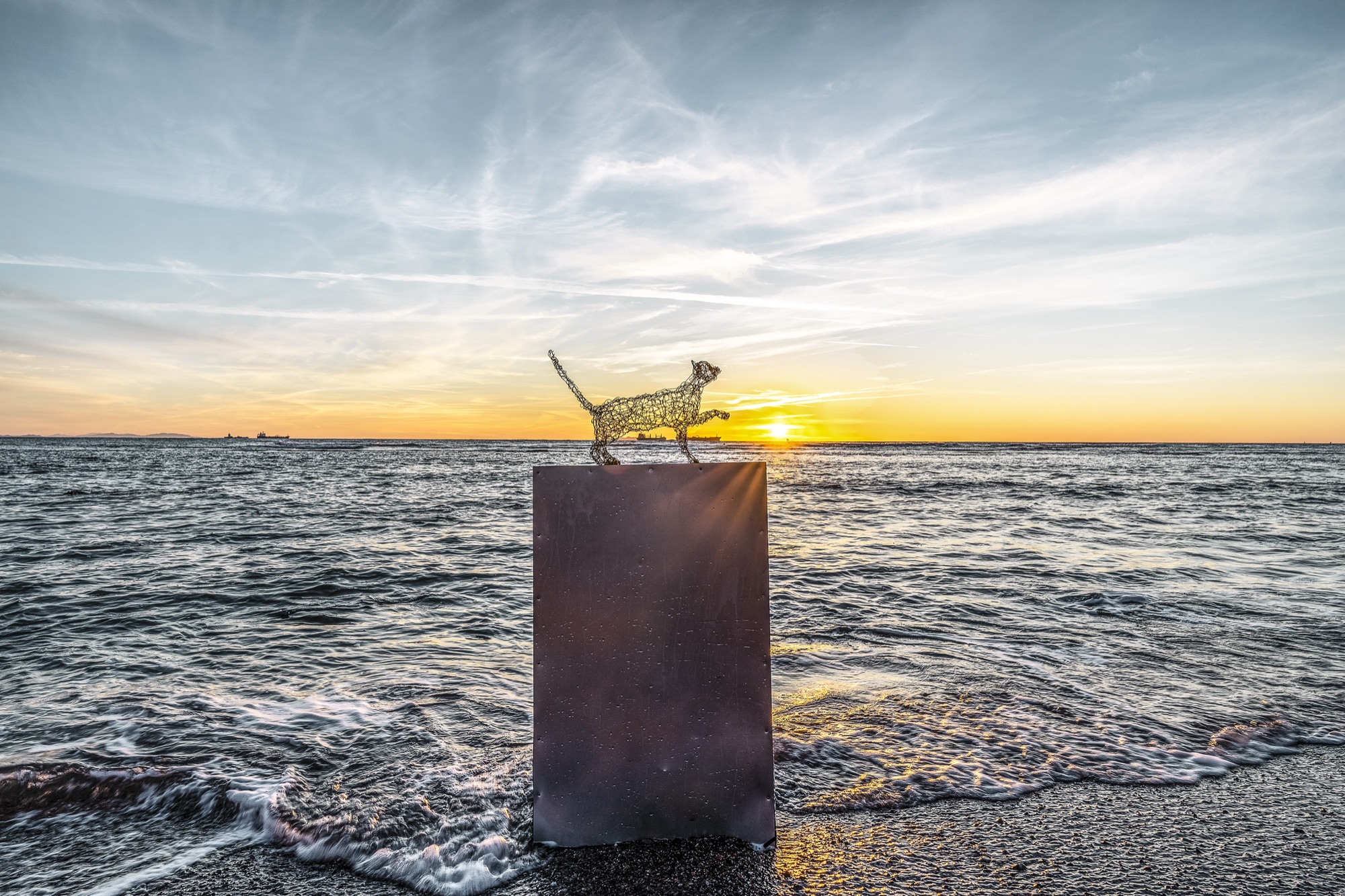 wire sculpure on a metal cube, standing from the sea in front of an orange sunset