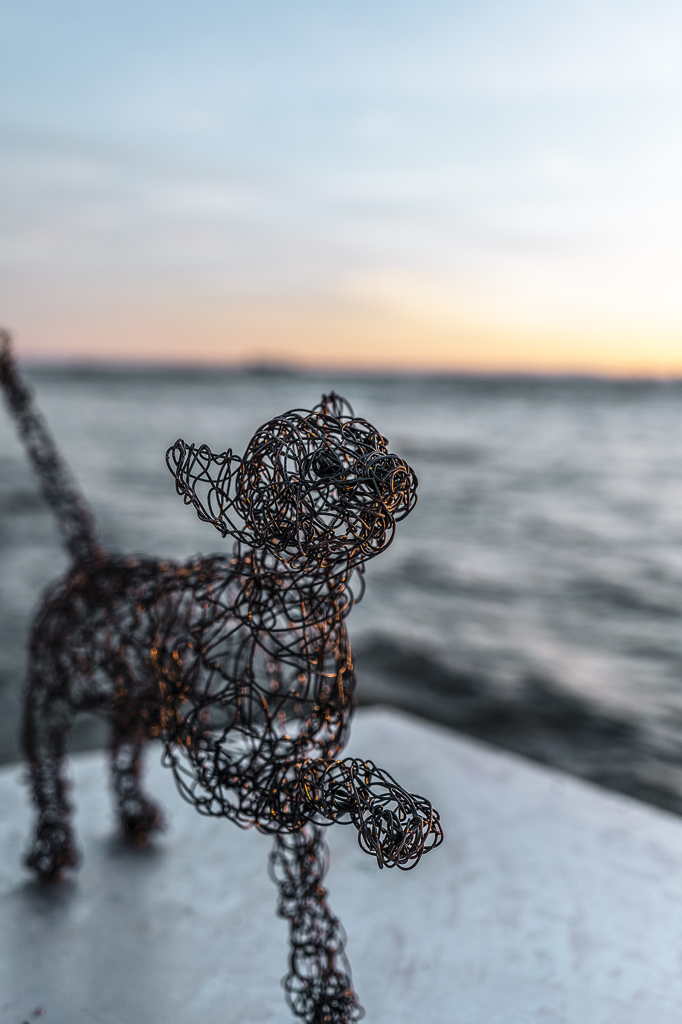 wire sculpure on a metal cube, standing from the sea in front of an orange sunset