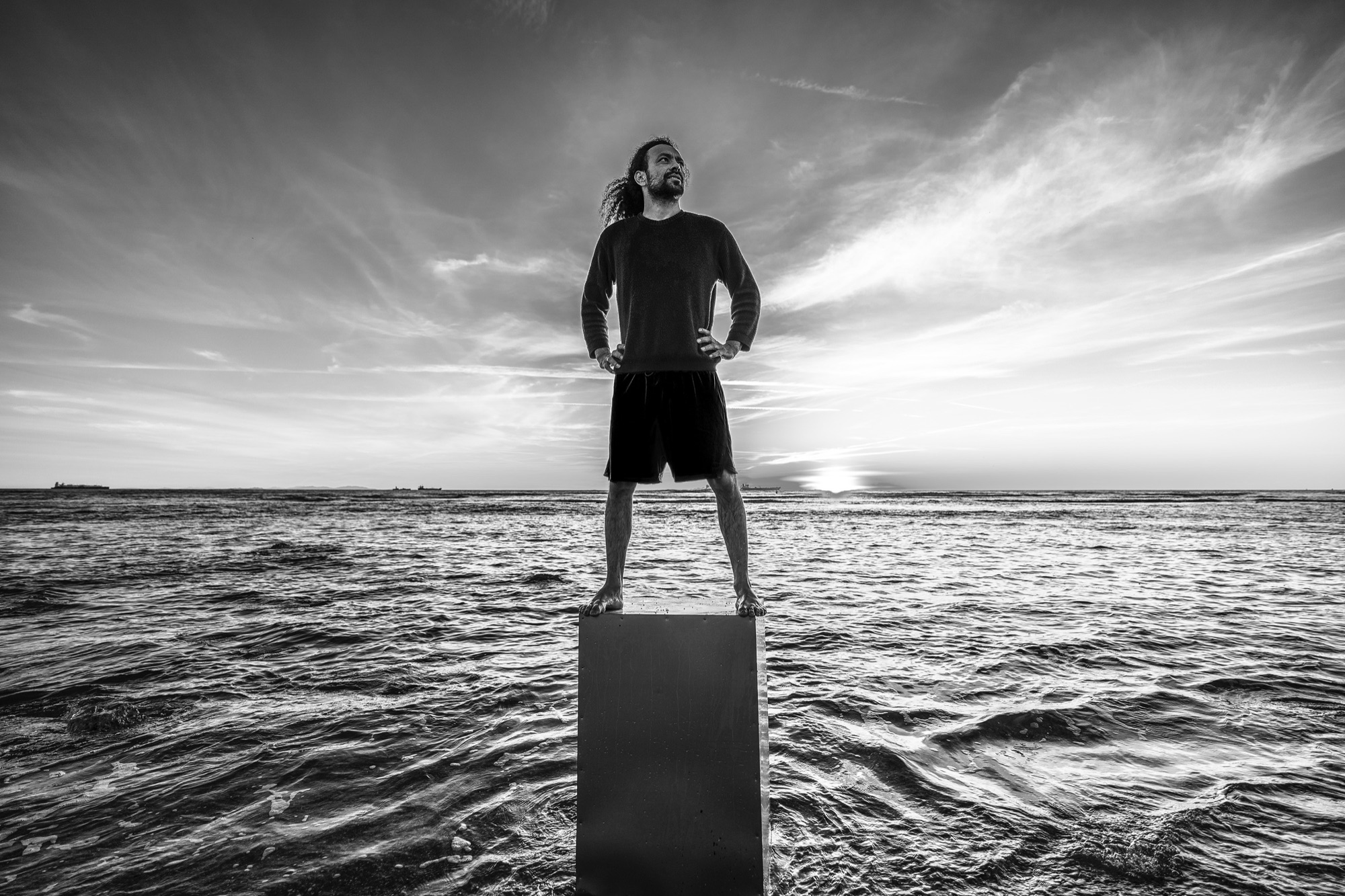 Rildson portrait on a metal cube, standing from the sea in front of an orange sunset. Black and white image.